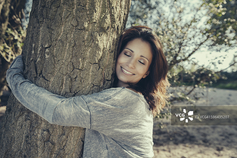 微笑的女人与闭着眼睛拥抱一棵树的肖像图片素材