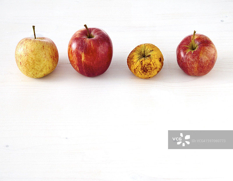 一行三个新鲜的苹果和一个干瘪的苹果在白木上图片素材