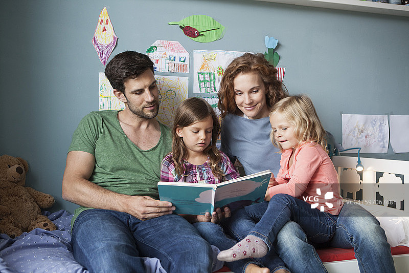 一对夫妇和小女儿一起坐在儿童房的床上看书图片素材
