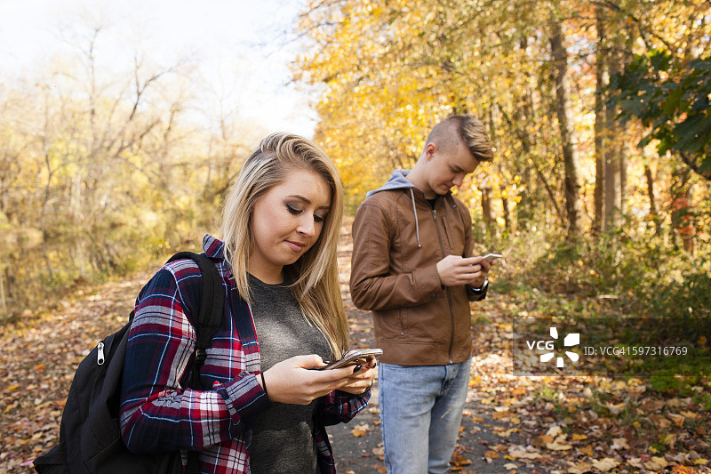 一个十几岁的男孩和一个成年的姐姐在秋天的森林里看手机短信图片素材
