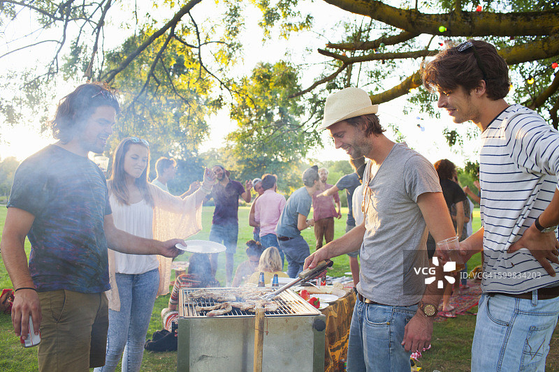 快乐的成年朋友在公园的日落派对上烧烤图片素材