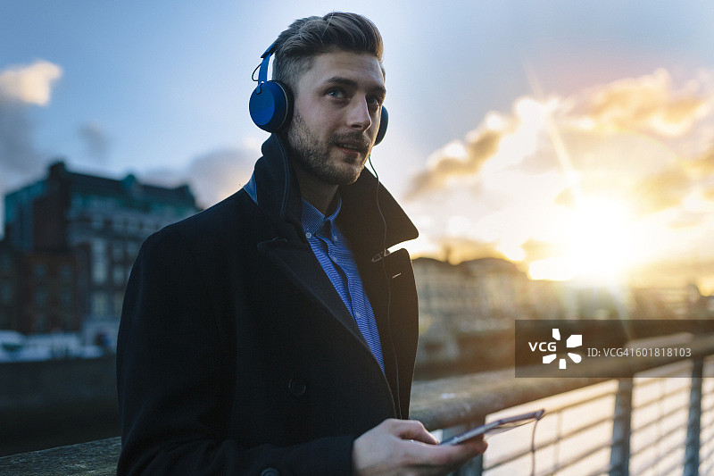 爱尔兰，都柏林，黄昏时分，年轻男子戴着耳机听音乐图片素材