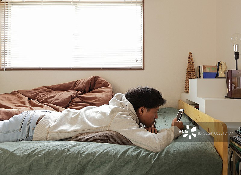 年轻人躺在床上玩手机图片素材