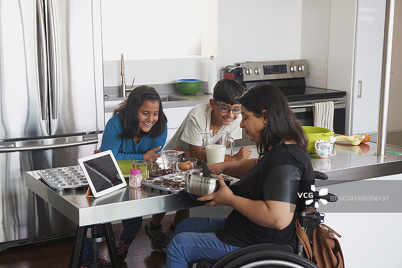 坐在轮椅上的印度母亲在厨房里和孩子们一起烘焙图片素材