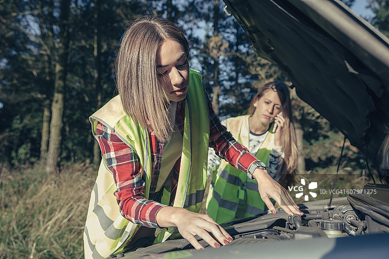 两名年轻女子穿着安全背心站在受损的汽车旁图片素材