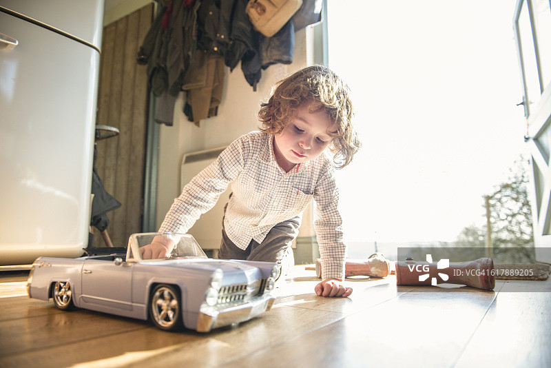 一个四岁的小男孩坐在后门玩玩具车图片素材