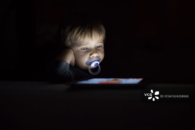 1岁的小男孩在黑暗中寻找数码平板电脑图片素材