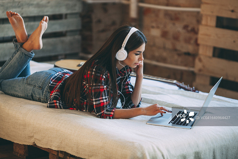 年轻女子在家里的床上用笔记本电脑听音乐图片素材