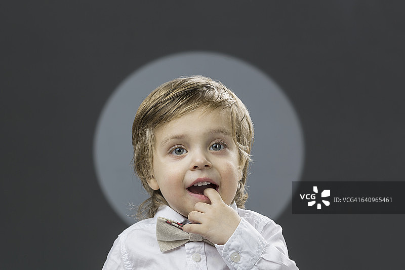 肖像可爱的男孩与手指在嘴的灰色背景图片素材