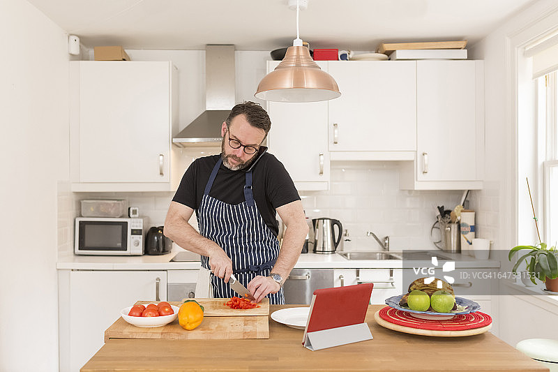 一名男子在厨房准备蔬菜时用智能手机打电话图片素材