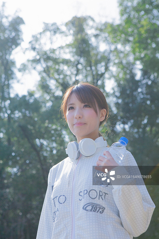 一个日本女人用一个塑料瓶在公园里拿着耳机图片素材