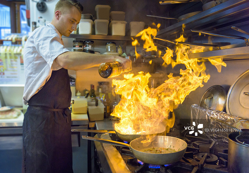 在传统的意大利餐厅厨房，厨师将白兰地倒入燃烧的锅中图片素材