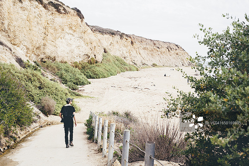 后视图的男性摄影师漫步到海滩，水晶湾州立公园，拉古纳海滩，加州，美国图片素材