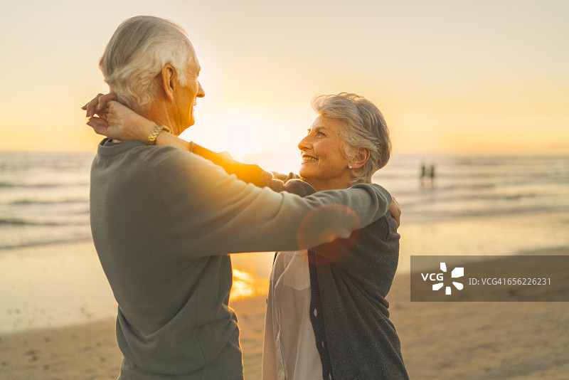 日落时分，一对老年夫妇在海滩上拥抱图片素材