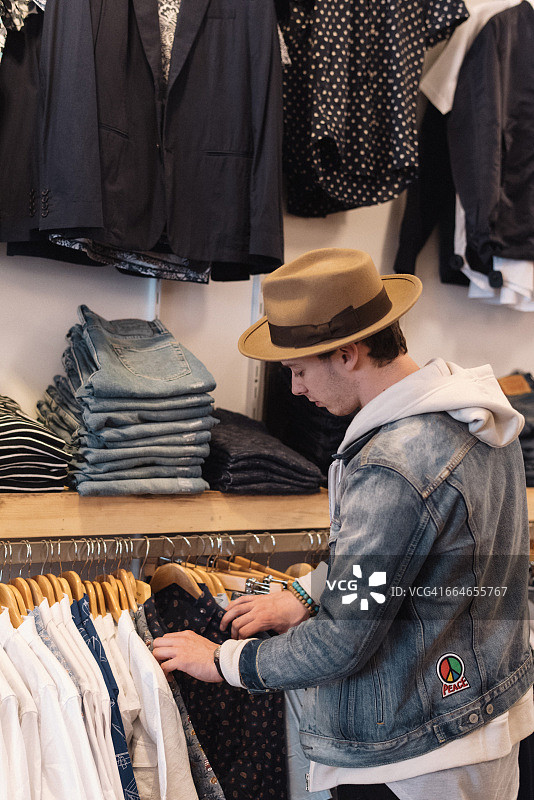 年轻男子在服装店的衣架上翻看衬衫图片素材