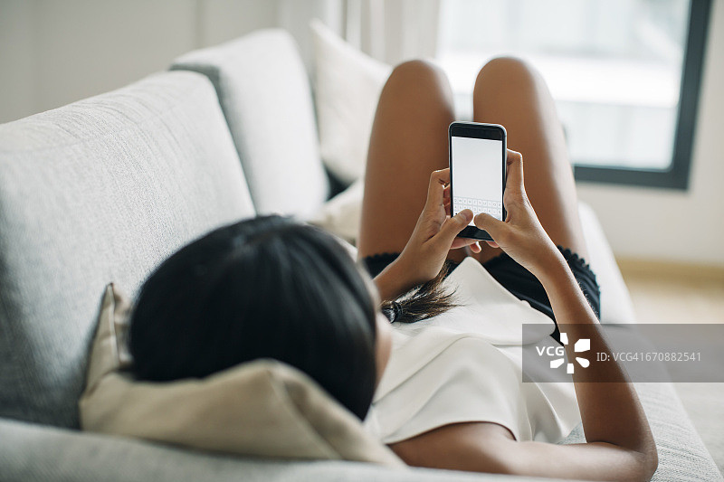 年轻女子躺在沙发上玩手机图片素材
