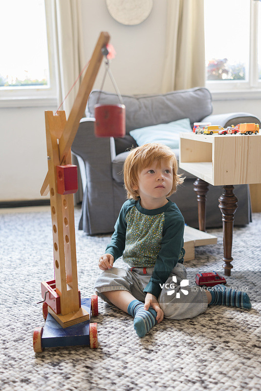 蹒跚学步的小男孩在地板上玩木制起重机玩具图片素材