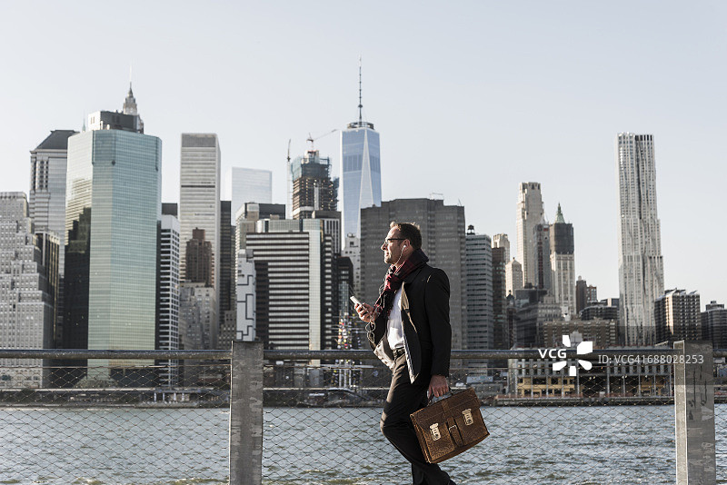美国，布鲁克林，商人拿着公文包站在曼哈顿的天际线前图片素材