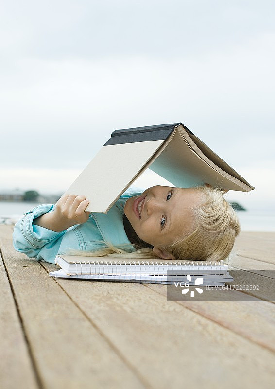 女孩躺在码头上，头上顶着书图片素材