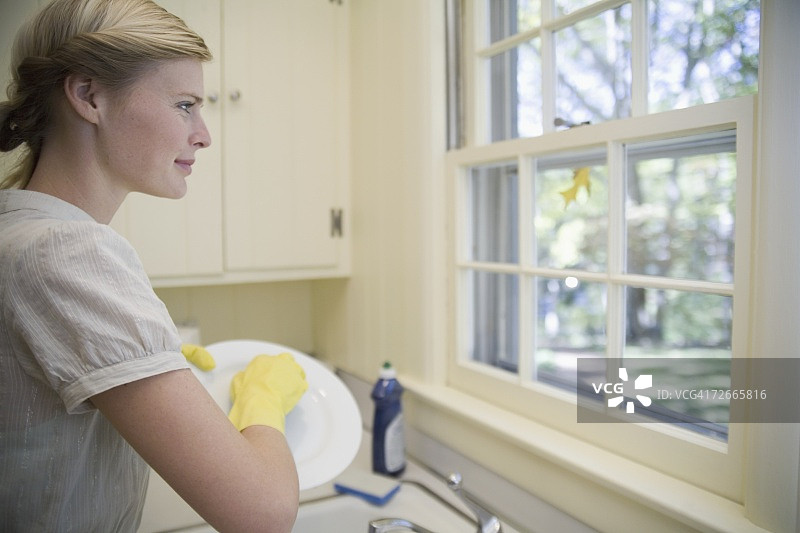 一个女人在洗陶器，从窗户往里看图片素材