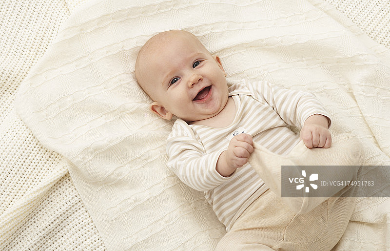 女婴(3-6个月)躺在毯子上，面带微笑图片素材