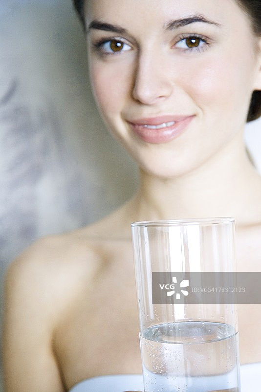 年轻女子拿着一杯水，对着镜头微笑图片素材