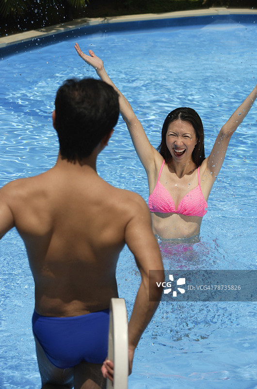 女人在游泳池里，双臂伸展着，看着站在她面前的男人图片素材