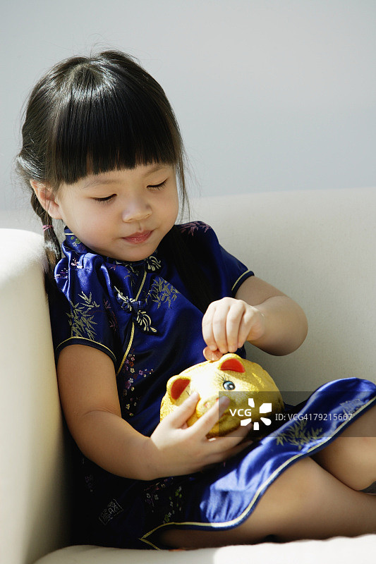 一个穿着蓝色丝绸旗袍的小女孩在玩存钱罐图片素材