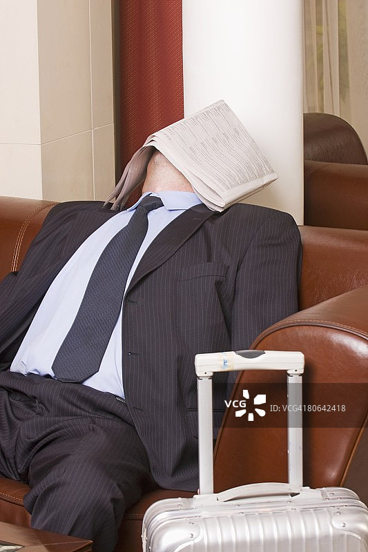 商人在酒店大厅打瞌睡，脸上盖着报纸图片素材