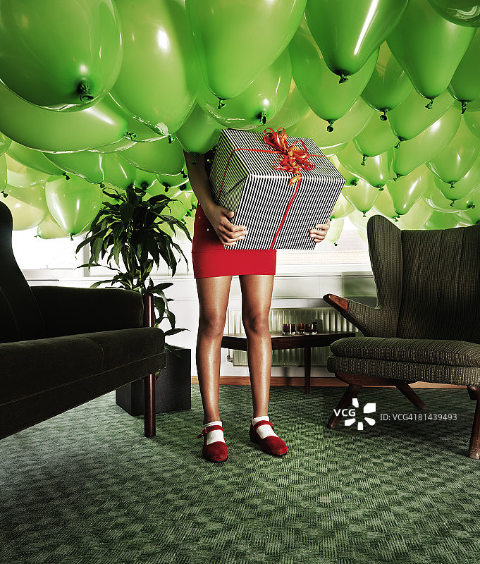 女孩拿着礼物在一个装满气球的房间里图片素材