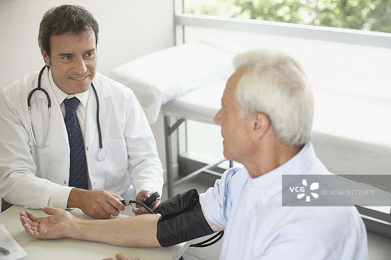 医生坐在办公室里，微笑着给病人量血压图片素材