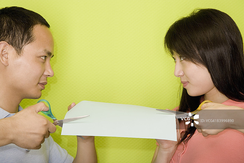 一个年轻的男人和一个年轻的女人用剪刀剪一张纸的特写图片素材