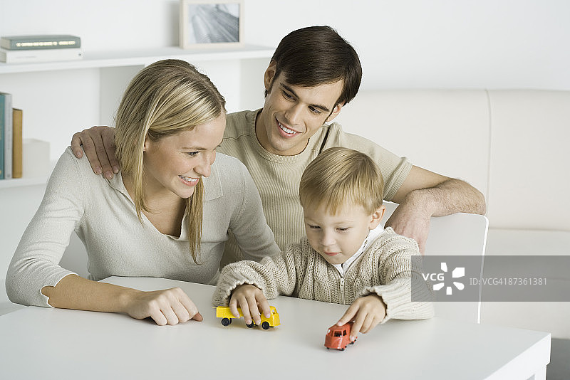 小男孩与父母坐在餐桌旁，玩着玩具卡车图片素材