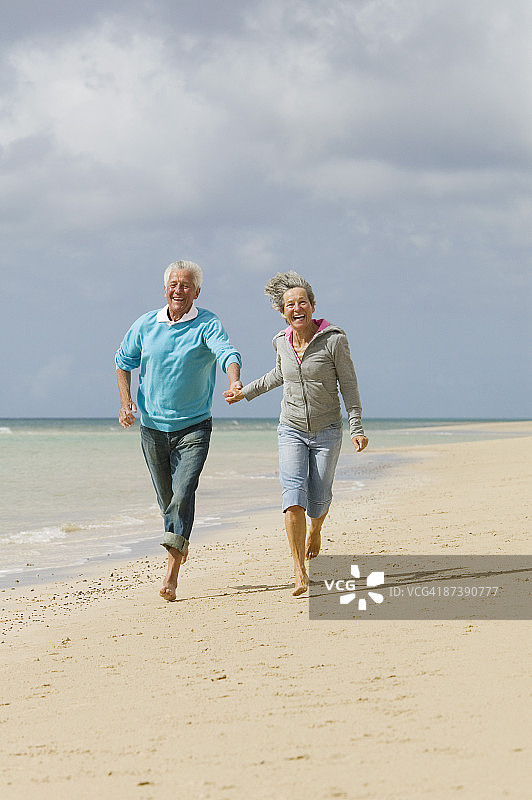成熟的夫妇手牵手在海滩上奔跑图片素材