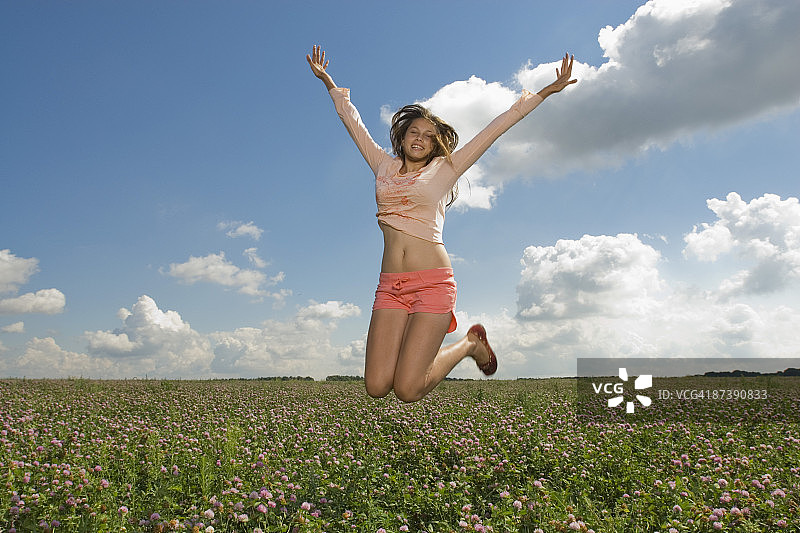 少女在夏日草地上跳跃图片素材