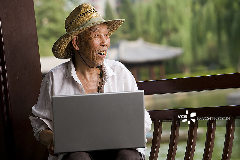 戴着草帽和手提电脑的老人在户外图片素材