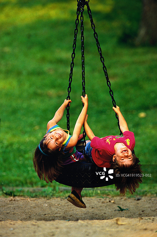 两个女孩(5-7)躺在公园的轮胎秋千上图片素材
