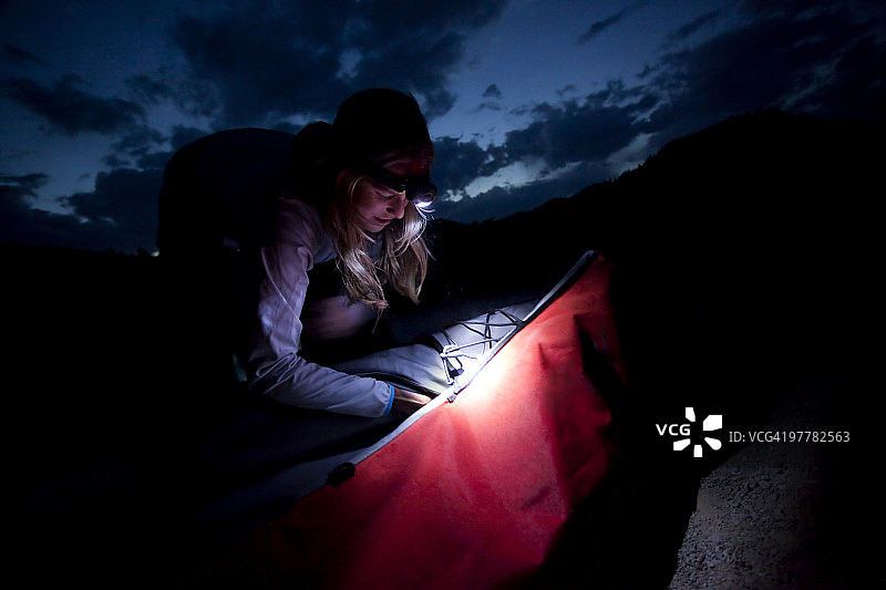 黄昏时分，一名女子在湖上游玩后，头戴大灯，正在清理她的皮艇。图片素材