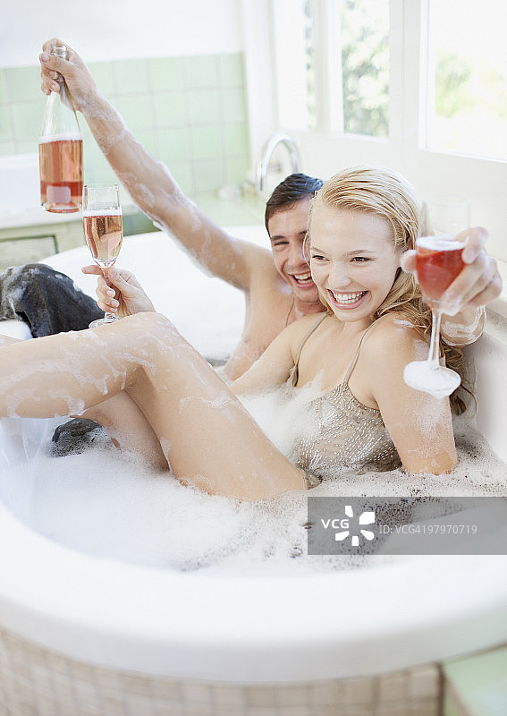 穿着衣服在浴缸里喝香槟的夫妇图片素材
