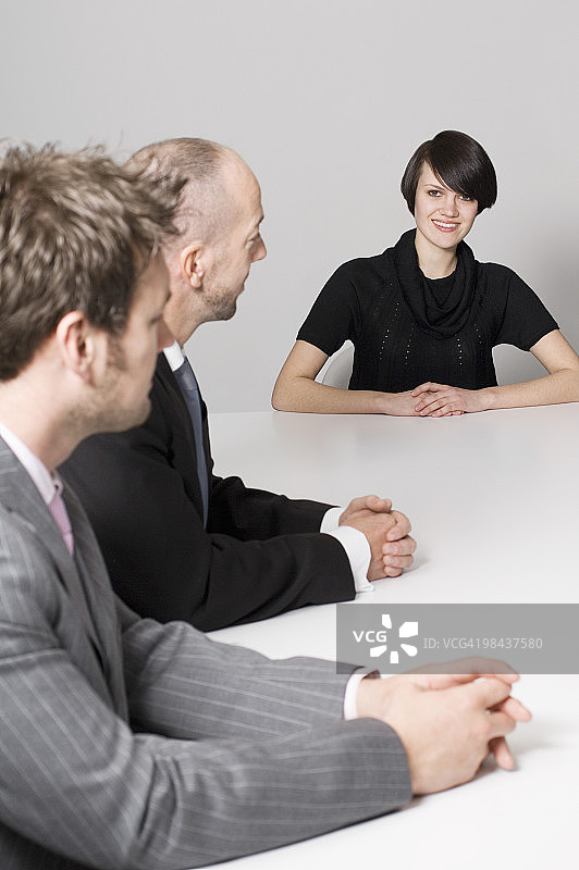一位年轻女子和两位商人坐在会议桌旁图片素材