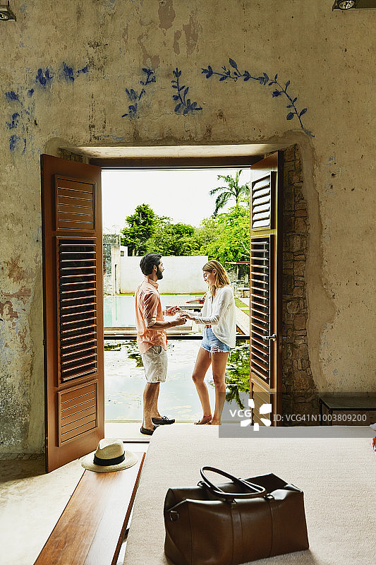 微笑的情侣手牵着手站在房间阳台俯瞰豪华的热带度假庭院图片素材