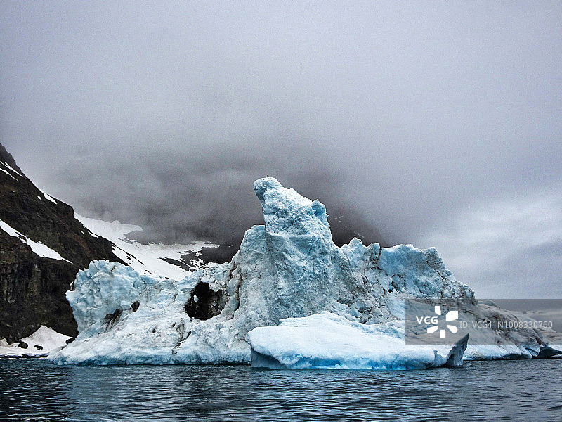 形状粗糙的冰山，以雾和山为背景。图片素材
