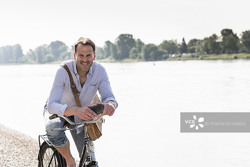 在莱茵河岸边，一个拥有自行车和智能手机的成熟男人图片素材
