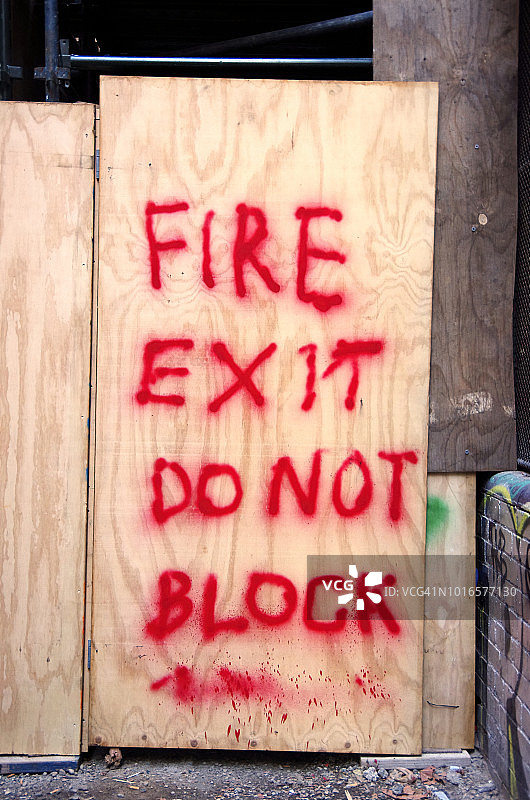 在通往建筑工地的临时胶合板门上，喷涂着“防火出口:请勿阻挡”的标志图片素材