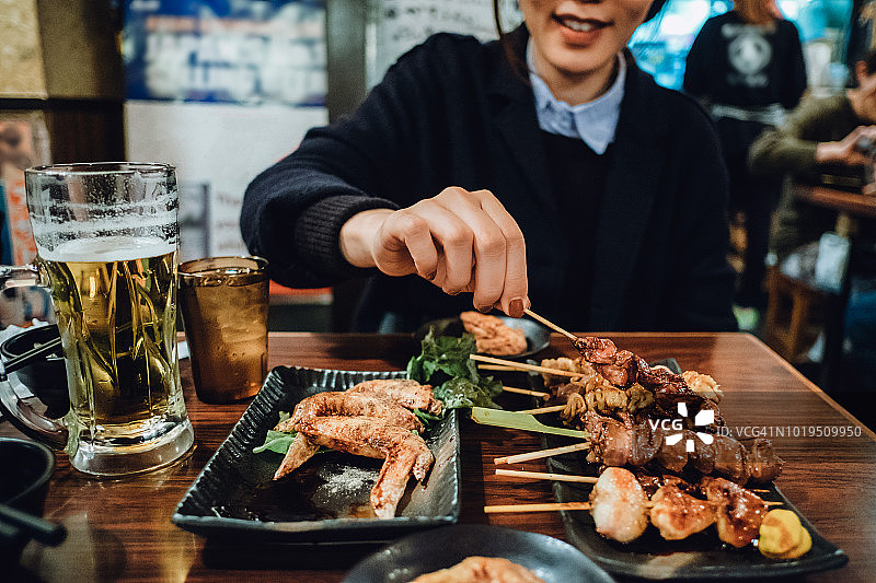 裁剪图像的女人享受传统日本烤肉和喝啤酒在日本风格的餐厅图片素材