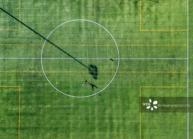 一个孤独的足球运动员在一个绿色的足球场上从上到下的鸟瞰图踢球图片素材