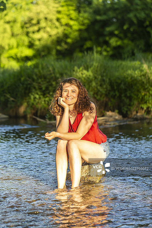 年轻女子坐在河边的石头上图片素材