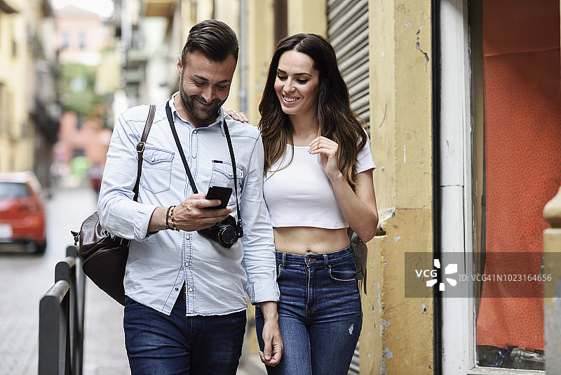 微笑的游客夫妇拿着手机走在城市里图片素材