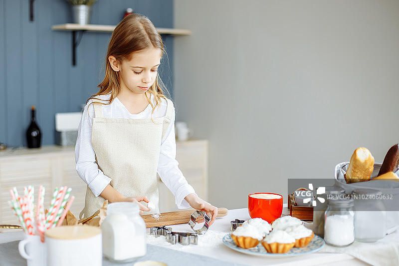 穿着围裙的可爱小女孩在厨房做饼干。图片素材