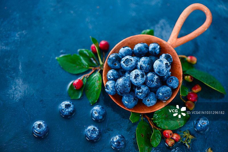 蓝莓在手工木勺在夏天的雨在蓝色的背景与复制空间。小世界的概念。秋收美食摄影图片素材